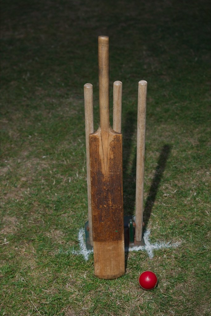 A cricket bat, ball, and stumps set up on a grass pitch